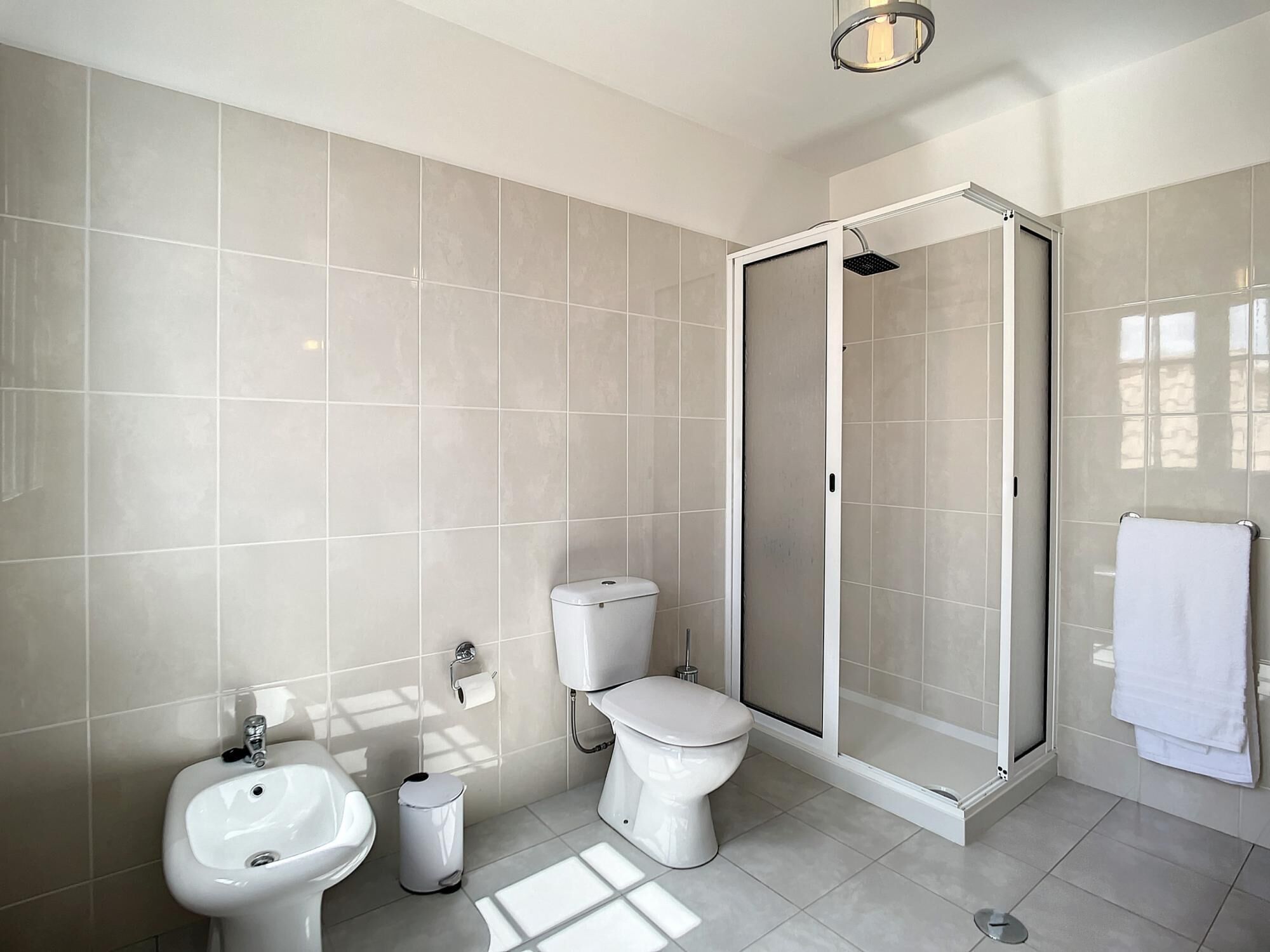 A modern bathroom with a toilet, bidet, sink, and a glass-enclosed shower area.