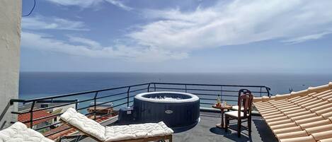Une terrasse sur le toit avec des chaises longues, un jacuzzi et une table avec des boissons.