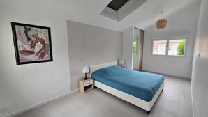 Ein Schlafzimmer mit Bett, Nachttisch, Wandbild, Dachfenster und Fenster.
