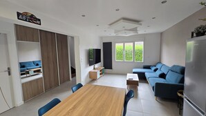 Ein modernes Wohnzimmer mit einem Holzesstisch, blauen Sofas, einem Fernseher und einem Kühlschrank.