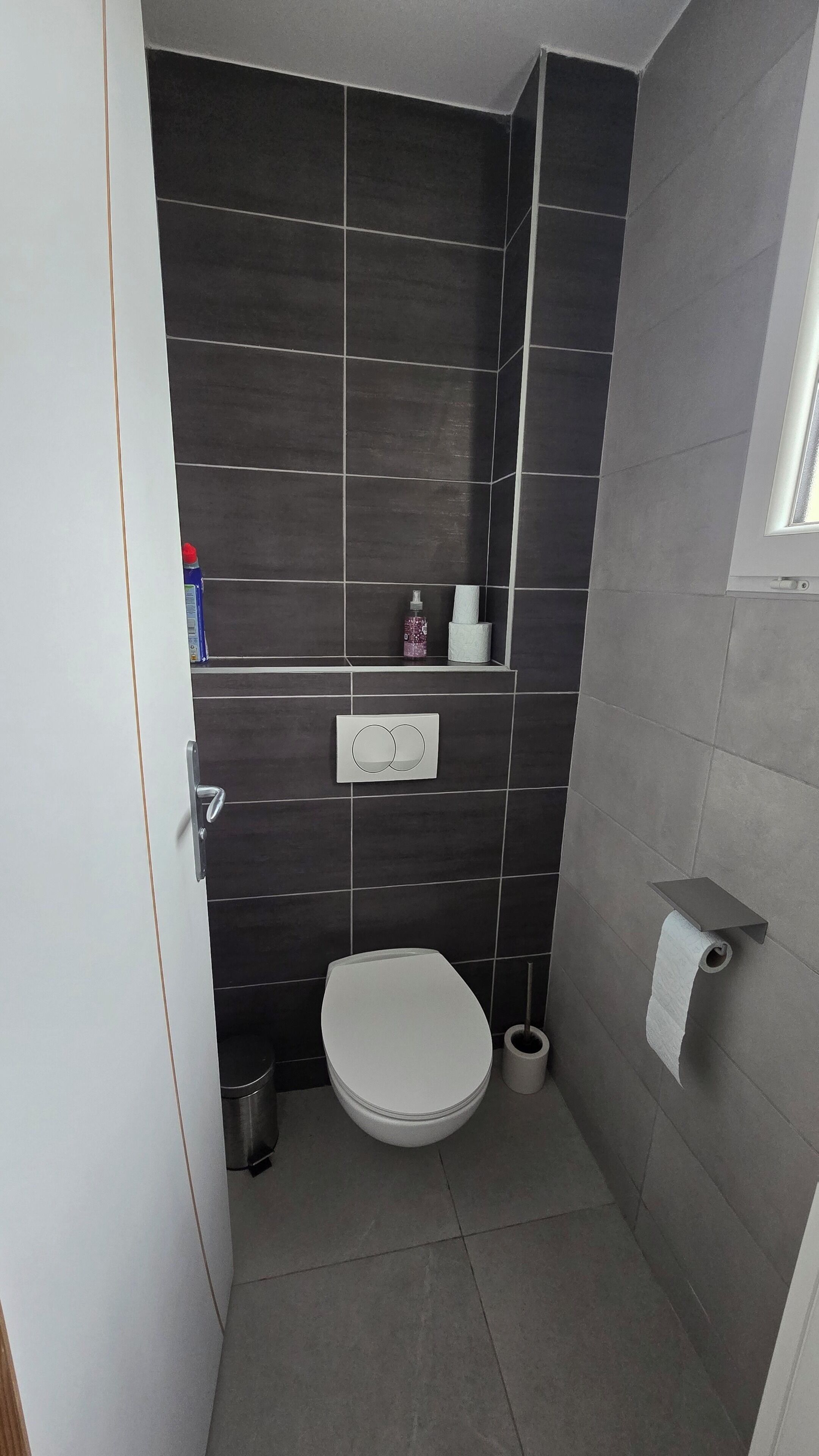 Une petite salle de bain moderne équipée de toilettes, d’un sèche-mains, d’une poubelle et d’un porte-serviettes.