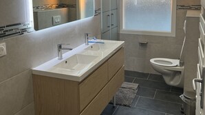 Ein modernes Badezimmer mit einem Doppelwaschbecken, einer Toilette und einem großen Fenster mit Milchglas.