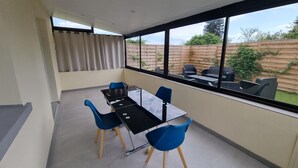 Ein modernes Zimmer mit einem Glastisch, blauen Stühlen und Blick auf den Garten durch große Fenster.