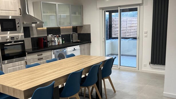 Eine moderne Küche mit einer zentralen Kochinsel, integrierten Geräten und einer Schiebetür zu einer Terrasse.