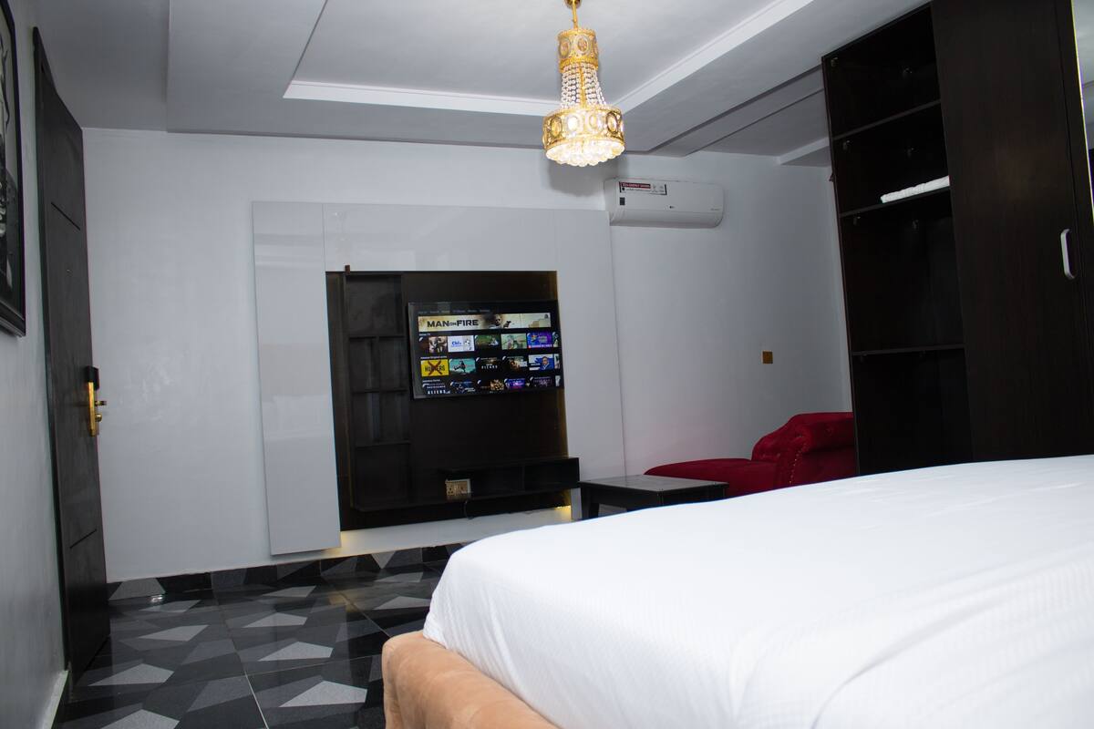 Ein Hotelzimmer mit einem Bett, einem an der Wand montierten Fernseher, einem roten Sessel und einer Deckenleuchte.