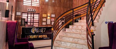 Zona de recepción de un hotel de lujo, con una escalera de mármol y un mostrador de recepción.