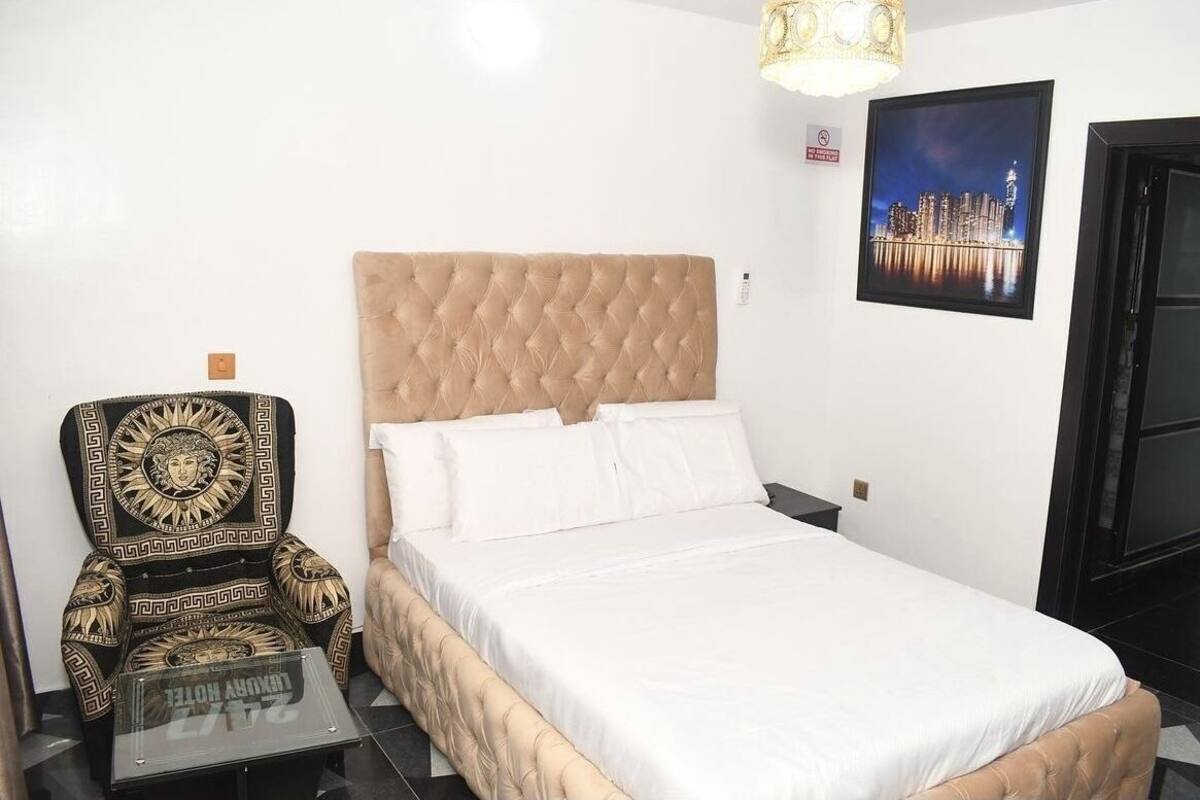 Ein Schlafzimmer mit einer gepolsterten Kopfteile, einem Bett mit weißen Leinentüchern, einem dekorativen Sessel und einem gerahmten Stadtbild an der Wand.