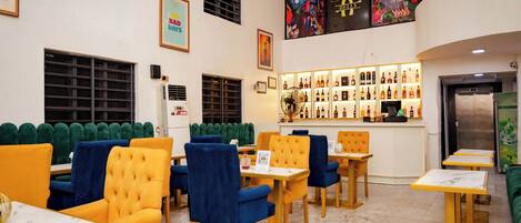 Un restaurante con asientos de tapicería verde y amarilla, una zona de bar con estantes llenos de botellas y un suelo de mármol.