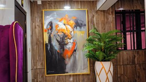 Een kamer met een groot abstract schilderij van een leeuw, een potplant en paarse gordijnen.