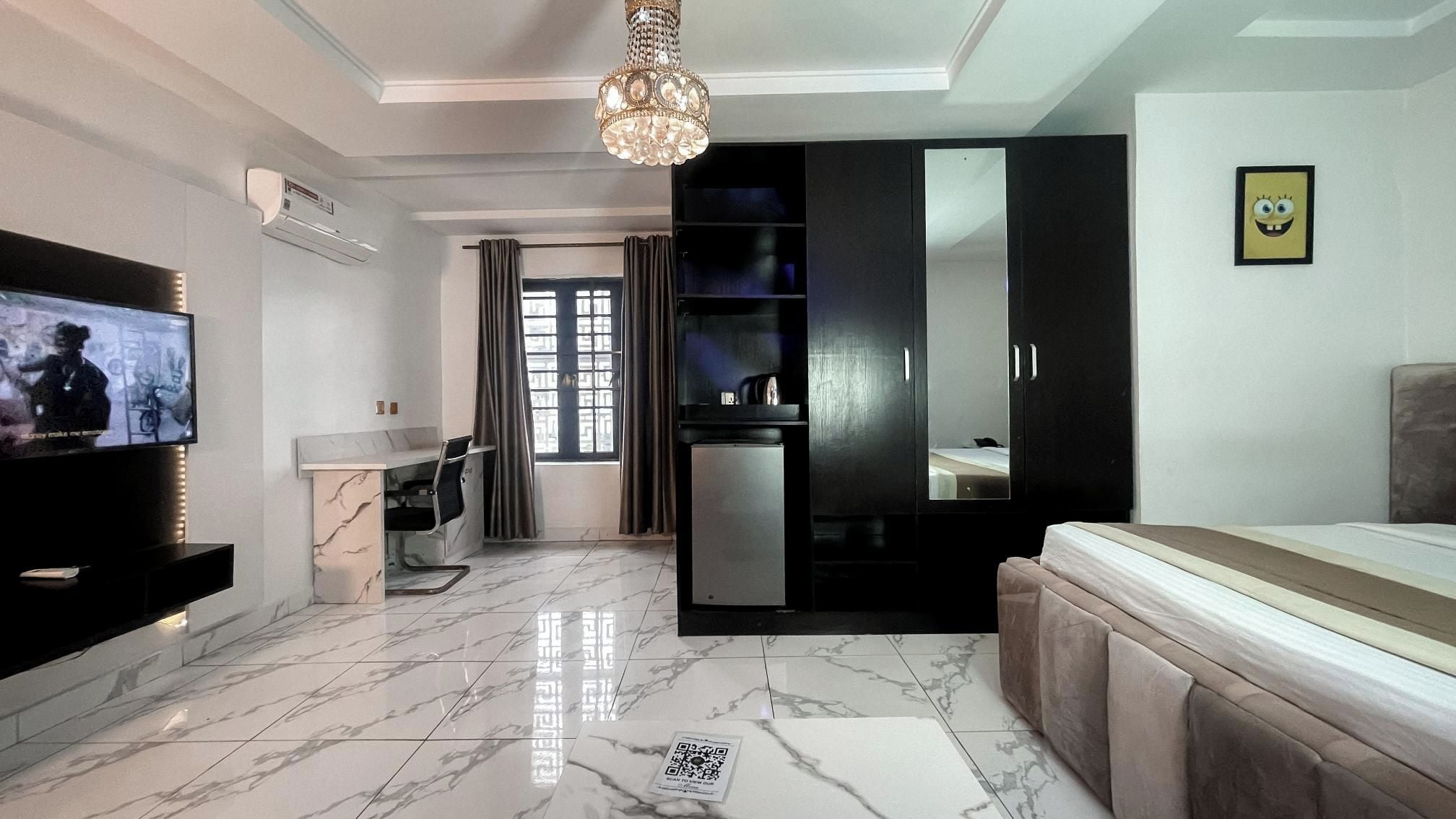 A modern living room with a flat-screen TV, a marble floor, a sofa, a dining area, and a kitchen with a refrigerator.