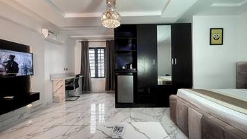 A modern living room with a flat-screen TV, a marble floor, a sofa, a dining area, and a kitchen with a refrigerator.