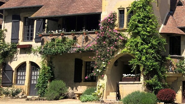 Una grande casa storica con una torre imponente, diversi balconi e un giardino curato.