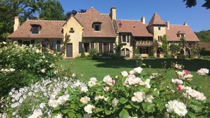Una grande casa storica con diversi camini, un prato curato e un giardino pieno di rose.