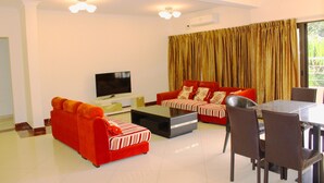 Uma sala de estar com um sofá vermelho, televisão, mesa de jantar com cadeiras e uma grande janela com cortinas.