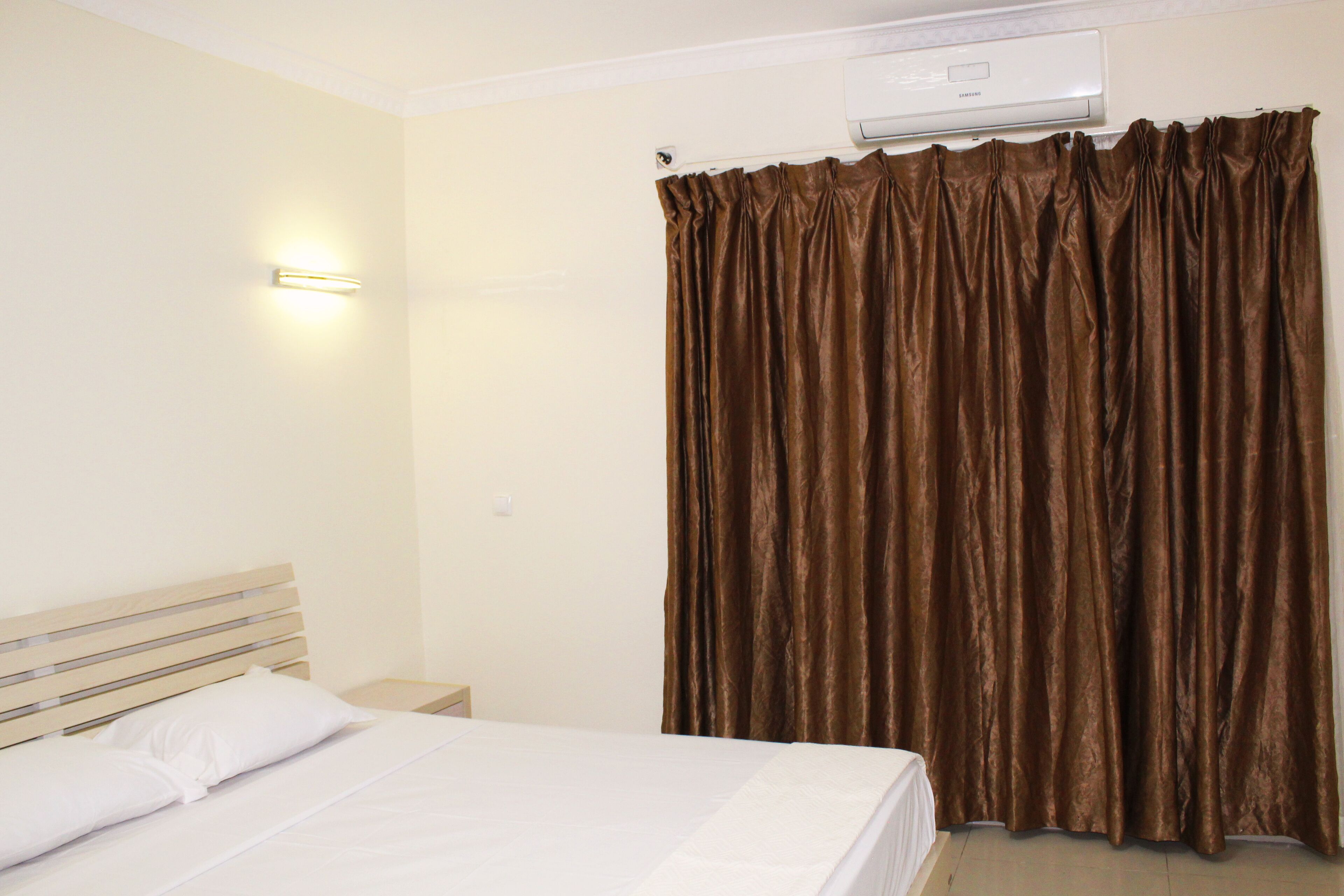 A hotel room with a bed, a nightstand, a wall-mounted air conditioner, and a curtain.