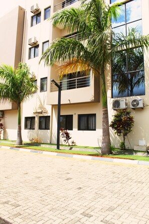 A multi-story building with air conditioning units, a palm tree, and a street with a curb. - Matola View Residence (Matola)
