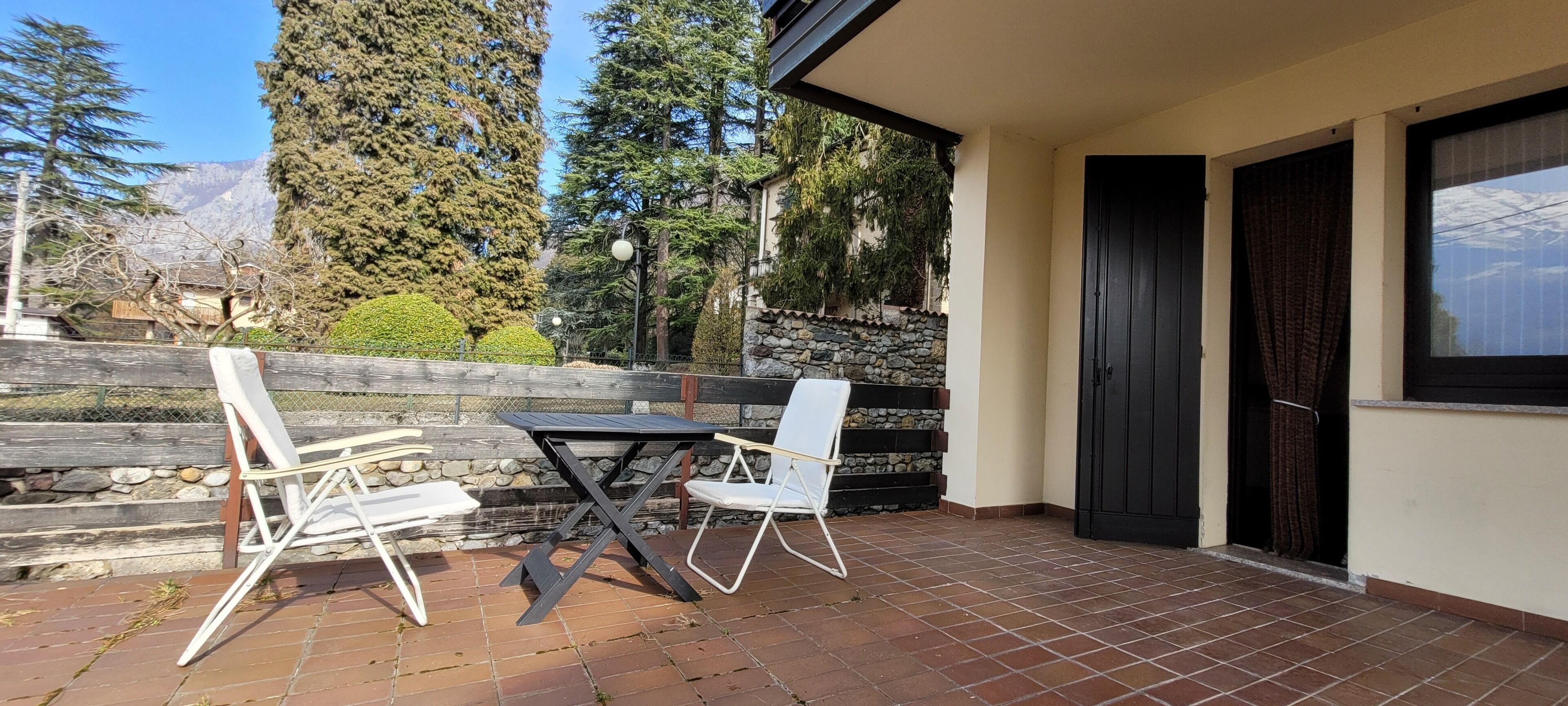A patio with a table and two chairs, a stone wall, and a view of trees and mountains.