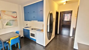 Cocina compacta con armarios azules, una pequeña mesa de comedor con sillas azules y un horno empotrado.