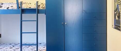 Un lit superposé avec une échelle, une armoire bleue avec plusieurs tiroirs et une affiche accrochée au mur.