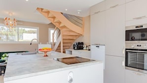 Una cucina moderna con isola centrale, forno a incasso e una scala che conduce a un piano superiore.