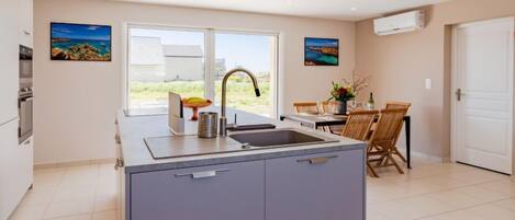 A modern kitchen with a large island, a dining area with wooden chairs, and a view of the outdoors.