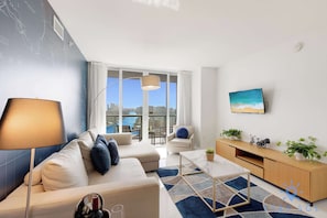 A modern living room with a sofa, a coffee table, and a view of a cityscape through large windows.