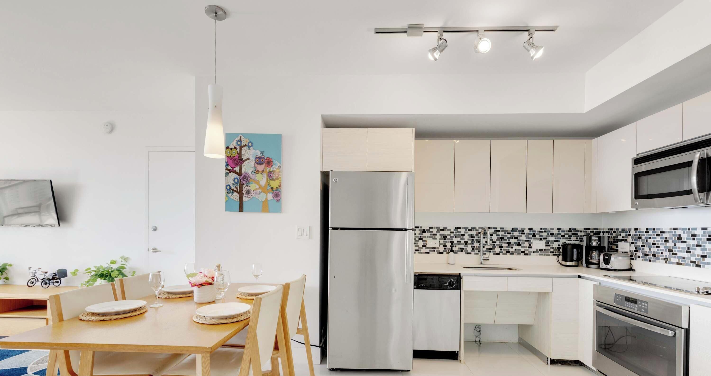 A modern kitchen with a dining area, stainless steel appliances, and a colorful wall art piece.