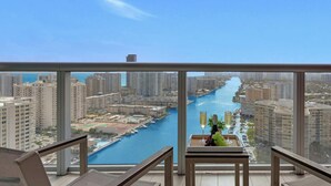 Ein Balkon mit Blick auf einen Fluss und die Skyline, ein Tisch mit einer Flasche und Trauben sowie zwei Stühle.