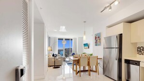 Eine moderne Küche mit einem Edelstahl-Kühlschrank, ein Essbereich mit Tisch und Stühlen sowie ein Blick auf die Stadt durch große Fenster.