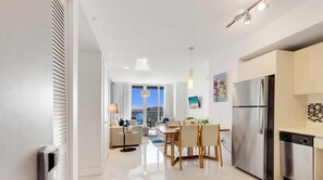 A modern kitchen with a stainless steel refrigerator, a dining area with a table and chairs, and a view of the city through large windows.