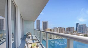 Ein Balkon mit Glastrennwand, einem Tisch mit Stühlen und Blick auf eine Skyline mit Hochhäusern.