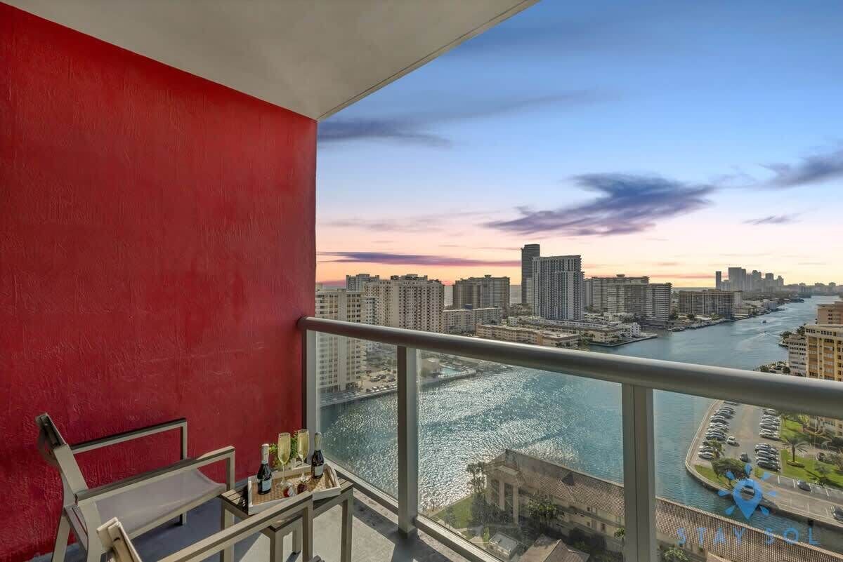 Ein Balkon mit roter Wand, Glasgeländer und Blick auf Stadt und Fluss.