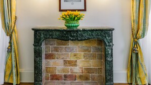 Una chimenea con un jarrón verde lleno de flores, dos luces fijadas a la pared y cortinas.