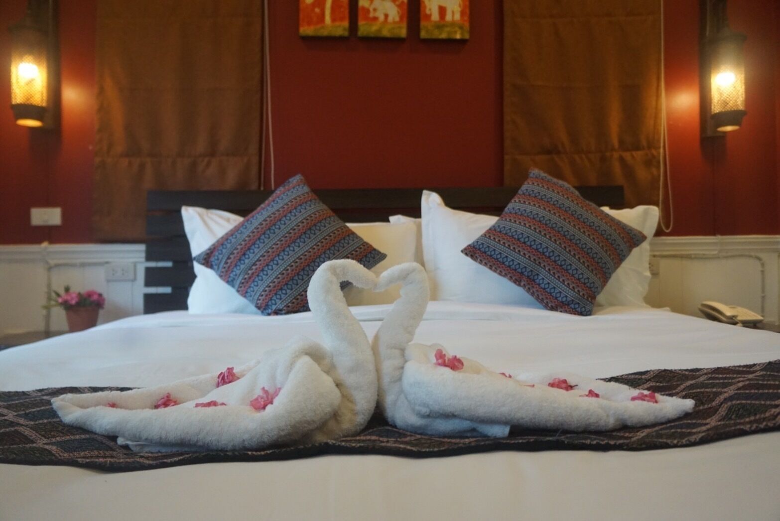 Una habitación de hotel con cama, almohadones decorativos, apliques de pared y un teléfono en la mesita de noche.