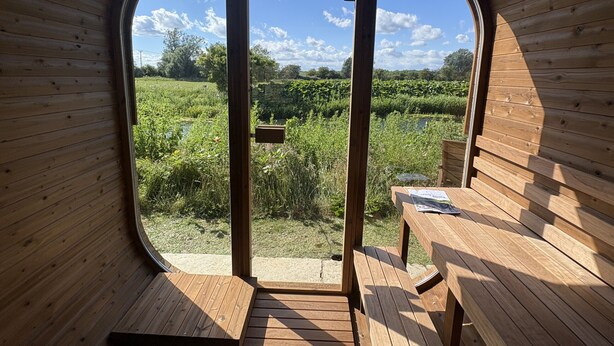 A wooden interior with a large circular window, wooden benches, and a view of a green landscape. - The Warren (Stamford)