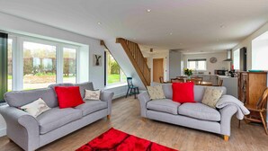 A spacious living room with two grey sofas, a red rug, and a staircase leading to a kitchen area. - The Warren (Stamford)