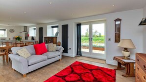 A spacious living area with a grey sofa, red rug, wooden furniture, and a view through large sliding doors to an outdoor garden. - The Warren (Stamford)