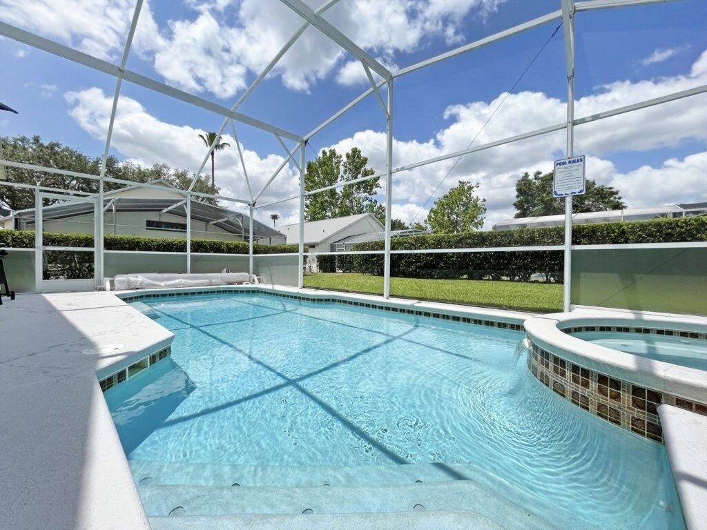 A swimming pool with a covered area, a hot tub, and a sign indicating pool rules.