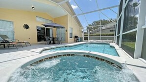 A swimming pool with a hot tub, lounge chairs, and a covered patio area.