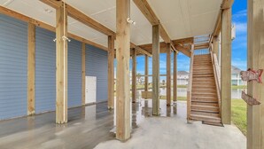 A covered outdoor area with wooden beams and a staircase leading to a deck. - Born To Beach 4 Bedroom Home by RedAwning (Port Bolivar)