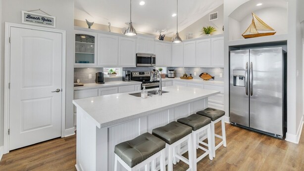 A modern kitchen with white cabinetry, a large island with bar stools, stainless steel appliances, and pendant lighting. - Born To Beach 4 Bedroom Home by RedAwning (Port Bolivar)