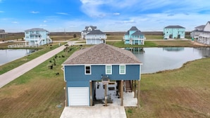 A residential area with houses on stilts over water, a clear sky, and a grassy landscape. - Born To Beach 4 Bedroom Home by RedAwning (Port Bolivar)