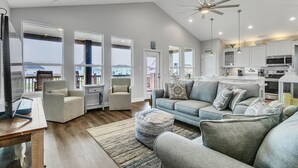 A spacious living room with a high ceiling, large windows, and a modern kitchen. - Born To Beach 4 Bedroom Home by RedAwning (Port Bolivar)