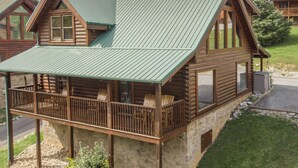 A log cabin with a balcony, stone foundation, and a green metal roof. - Pool Table | Pigeon Forge | Hot tub | Fireplace | Arcade | WiFi (Pigeon Forge)