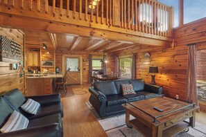 A cozy cabin interior with a wooden dining area, a black leather sofa, and a wooden coffee table.