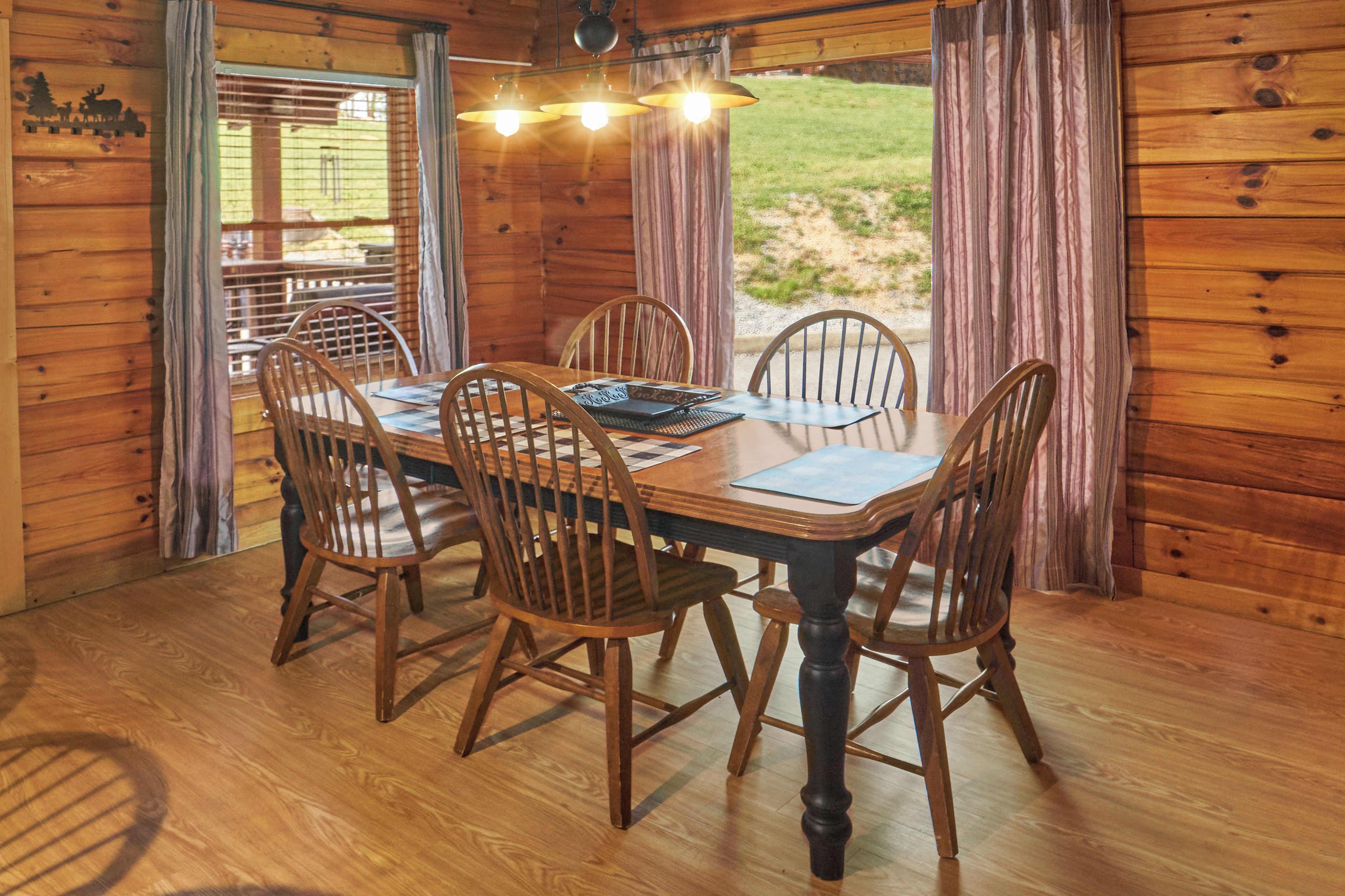 A wooden dining area with a table and chairs, a window with curtains, and a view of the outdoors.