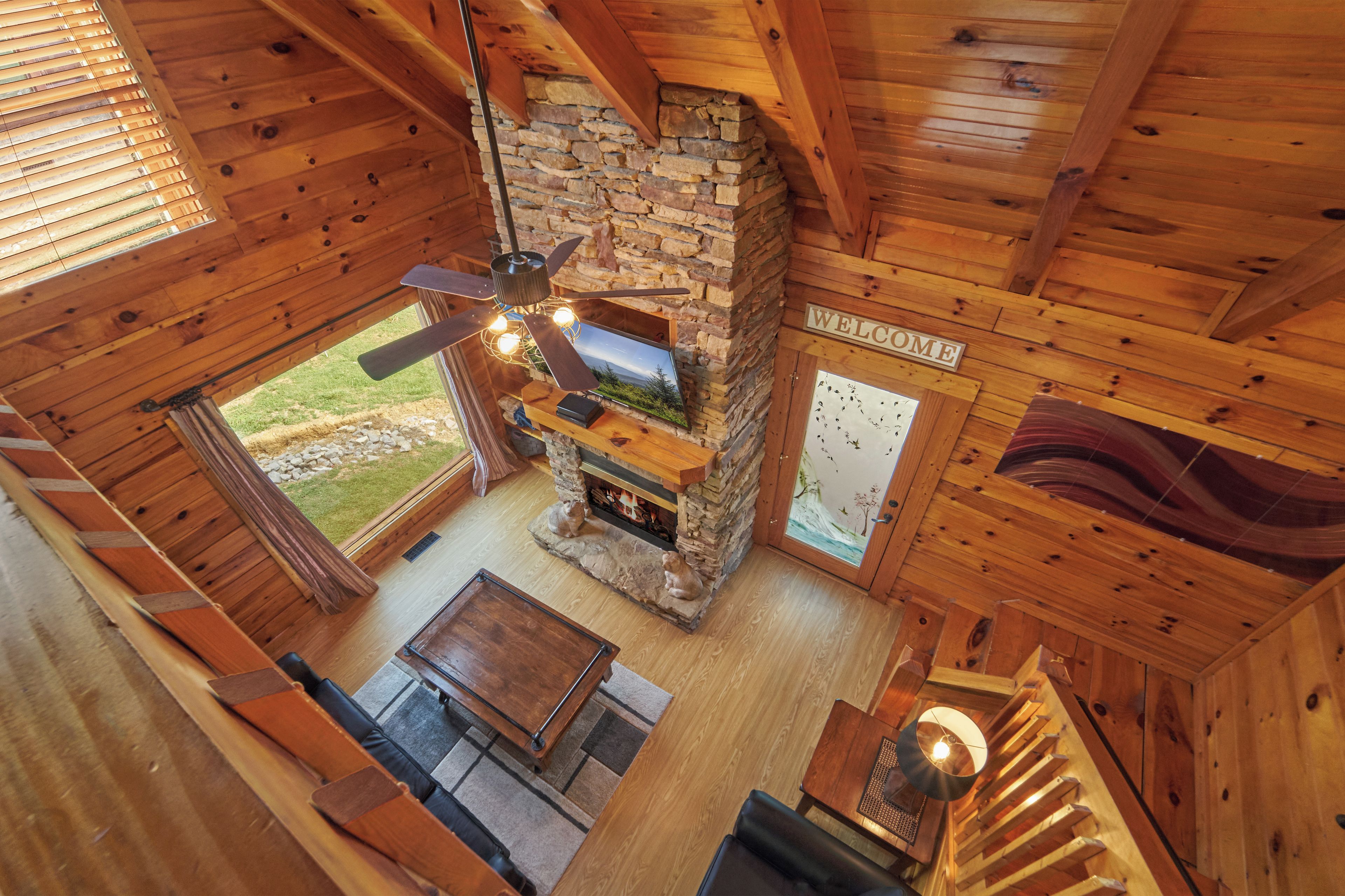 A log cabin interior with a stone fireplace, wooden ceiling beams, and a 'WELCOME' sign.