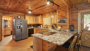 A cabin-style kitchen with wooden cabinets, a granite countertop, a built-in refrigerator, and a dining area with wooden chairs. - Pool Table | Pigeon Forge | Hot tub | Fireplace | Arcade | WiFi (Pigeon Forge)