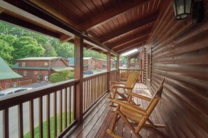 Een houten veranda met schommelstoelen, een leuning en een uitzicht op huisjes op de achtergrond.