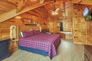 A wooden cabin bedroom with a bed, a desk, a chair, and a television.